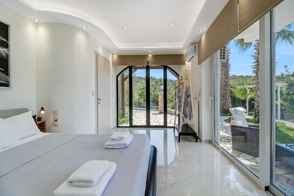 Una habitación de hotel moderna con una cama grande, vistas al exterior y una puerta de vidrio que da a un patio.