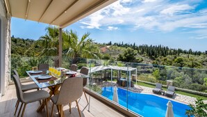 Un balcón con mesa de vidrio, sillas y una piscina.