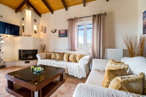 A cozy living room with a fireplace, white sofas, a coffee table, and a TV.