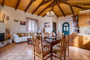 Un vaste espace de vie doté d’un plafond en bois, d’une table à manger avec des chaises, d’un canapé et d’un coin cuisine avec des meubles en bois.