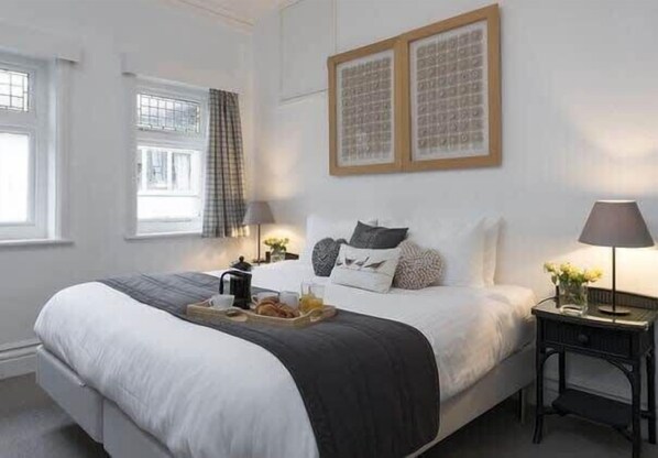 A neatly arranged bedroom with a large bed, bedside tables, and a window with curtains.