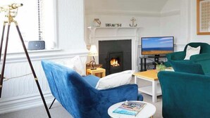 A living room with a fireplace, teal armchairs, a coffee table, and a television. - The Lookout - Beautiful sea views (Filey)