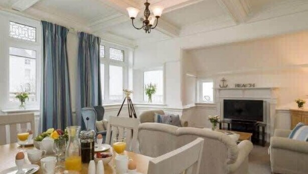 A dining area with a table set for breakfast, a sofa, and a television in the background. - The Lookout - Beautiful sea views (Filey)