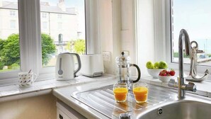 A kitchen with a stainless steel sink, a kettle, a coffee maker, and a bowl of fruit. - The Lookout - Beautiful sea views (Filey)