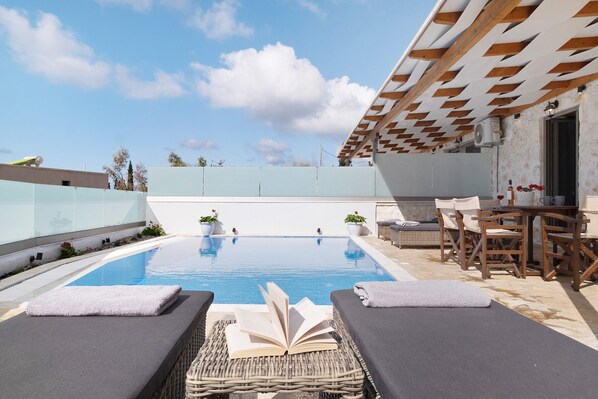 A rooftop pool area with lounge chairs, a table, and a pergola.