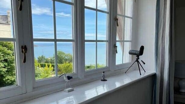 Ein Zimmer mit großem Fenster mit Blick auf ein Gewässer, einem Stativ und einem kleinen Stuhl.