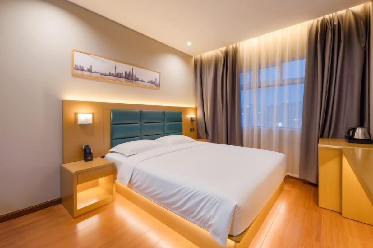 Una habitación de hotel con cama, mesita de noche, lámpara y un cuadro de un paisaje urbano en la pared.