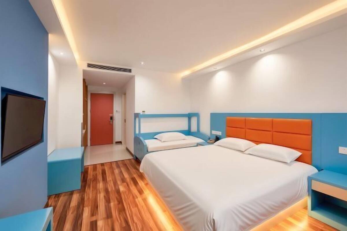 A hotel room with two beds, a TV, and a wooden floor.