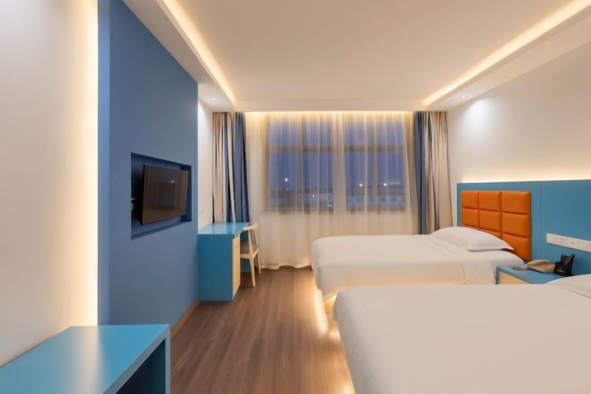 Habitación de hotel con dos camas, televisión, escritorio y ventana con cortinas.