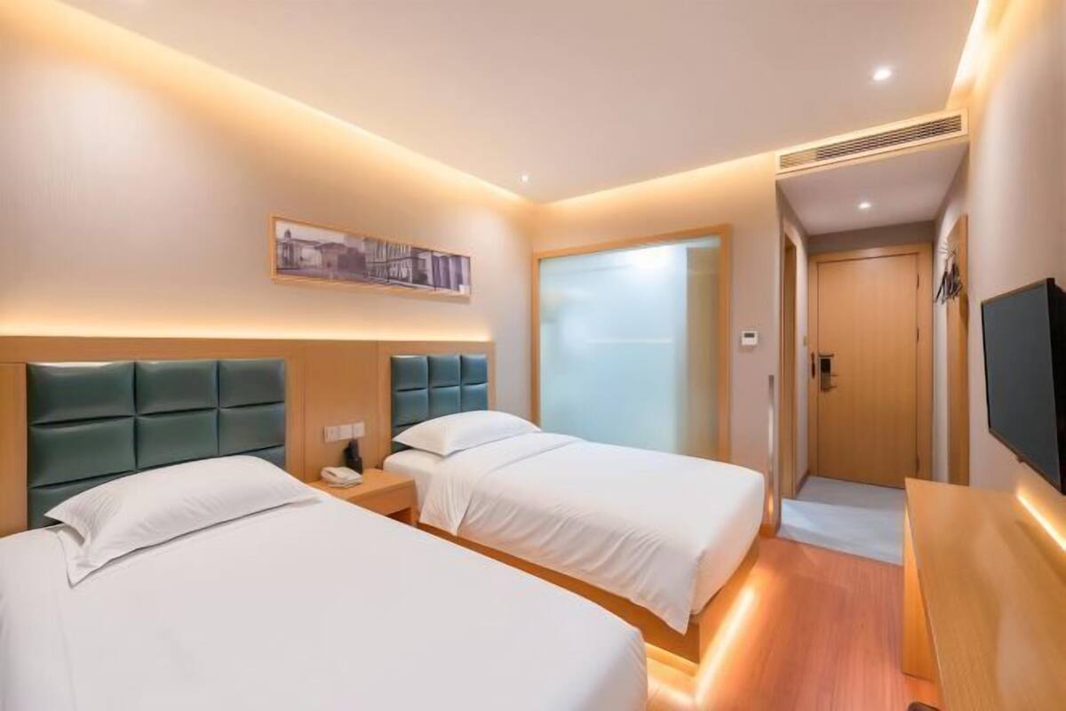 A hotel room with two beds, a bedside table with a lamp, a TV, and a door leading to a bathroom.