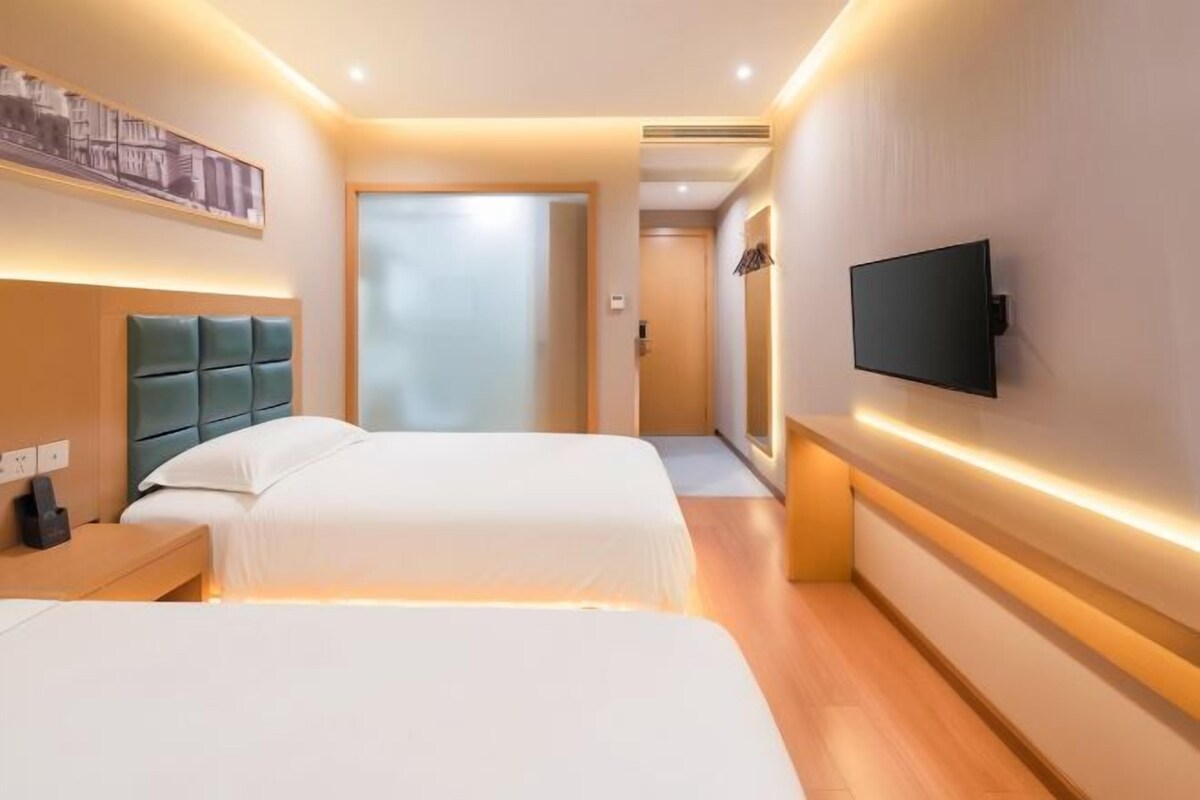 Habitación de hotel con dos camas, una televisión y un pasillo que da a otra habitación.