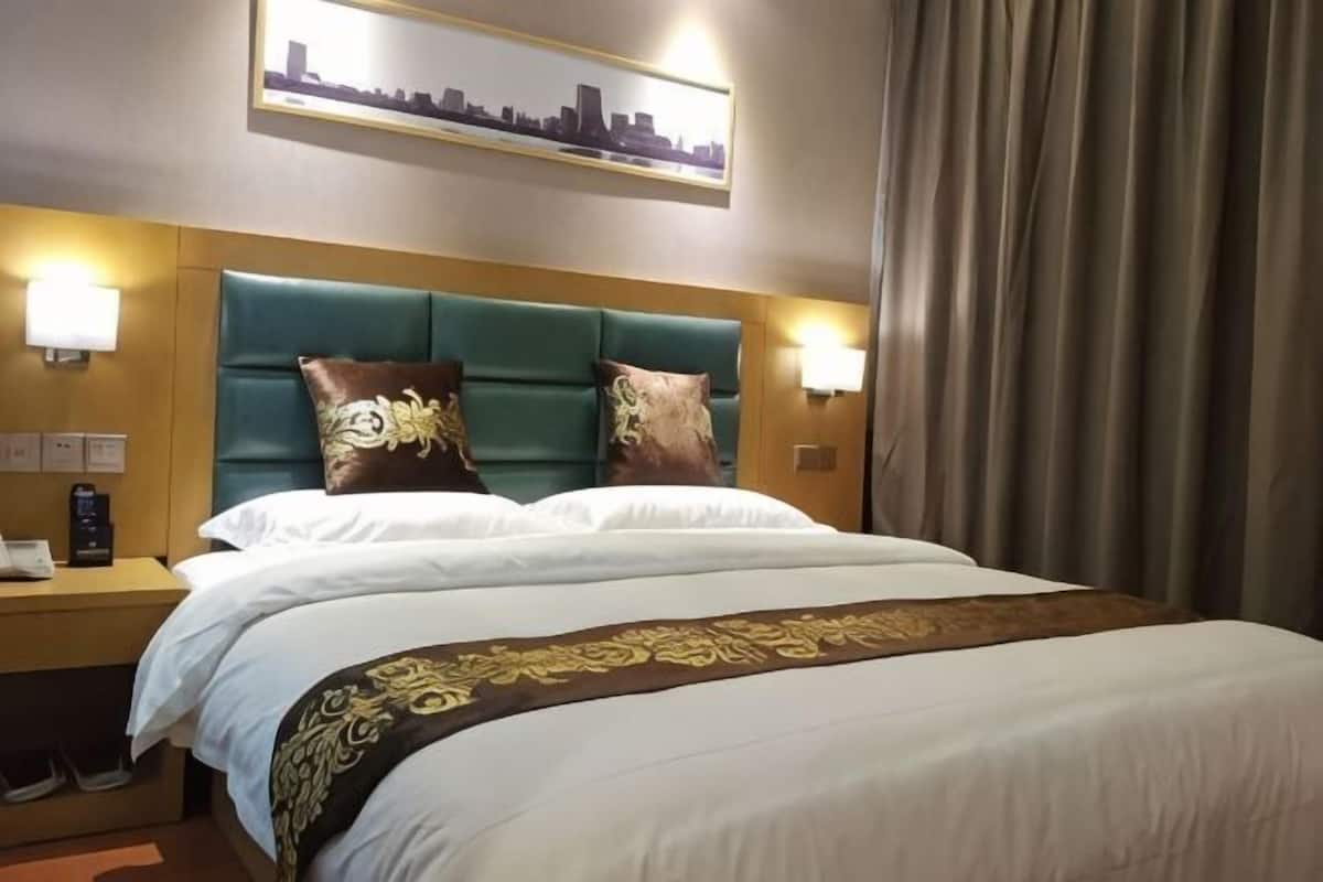 A hotel room with a bed, headboard, bedside tables, lamps, and a cityscape artwork on the wall.