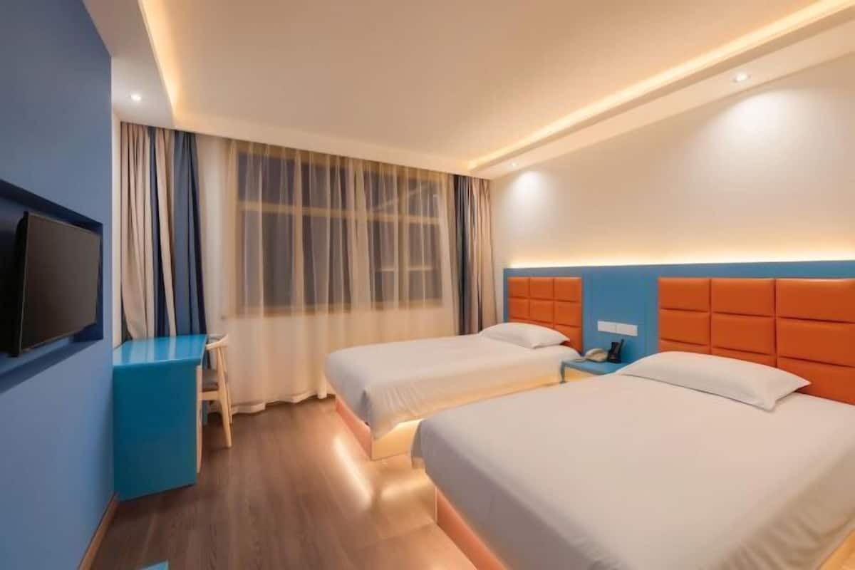 A hotel room with two beds, a desk, a TV, and a nightstand.