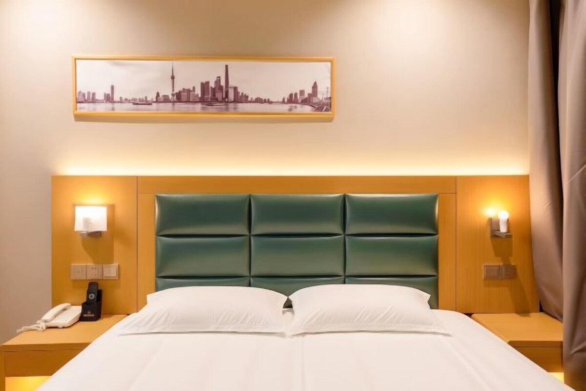 Una habitación de hotel con una cama, lámparas de noche, un teléfono y un cuadro con una vista urbana enmarcada en la pared.