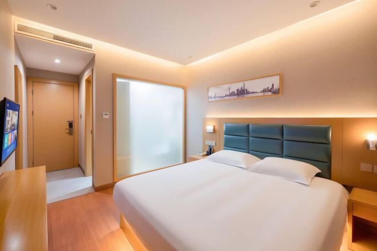 A hotel room with a large bed, a desk, a door, and a wall-mounted artwork.