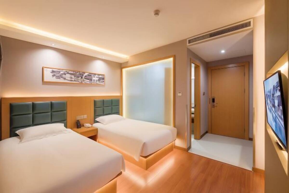 A hotel room with two beds, a nightstand, a television, and a framed picture on the wall.