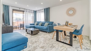 Una sala de estar moderna con un sofá azul, una mesa de comedor con sillas y un gran ventanal con cortinas.