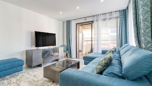 Una sala de estar moderna con televisor de pantalla plana, sofás azules, una mesa de centro de mármol y vistas a través de un ventanal.