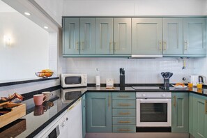A kitchen with teal cabinets, a microwave, an oven, and a coffee maker.