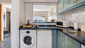 A compact kitchen with a washing machine, microwave, and a window with a view.