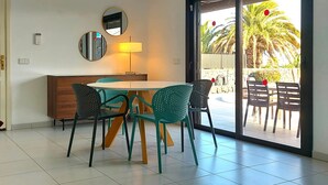 Ein Essbereich mit Tisch und Stühlen, einer Lampe, einem Spiegel und einer Schiebeglasdoor zum Außenbereich mit einer Palme.