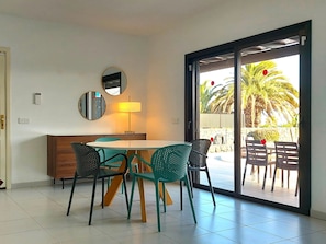 A dining area with a table and chairs, a lamp, a mirror, and a sliding glass door leading to an outdoor patio with a palm tree. - Vacation Home "Villa Fernando" with Sea View, Private Pool & Wi-Fi (Playa Blanca)