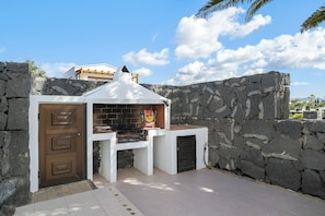 An outdoor barbecue area with a stone wall, a grill, and a door.
