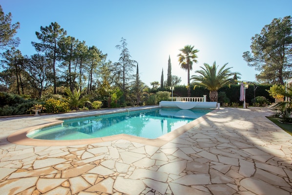 A swimming pool with a stone deck, surrounded by trees and a clear sky.