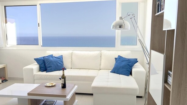 Ein modernes Wohnzimmer mit einem weißen Sofa, blauen Kissen, einem Couchtisch und einer Stehlampe.