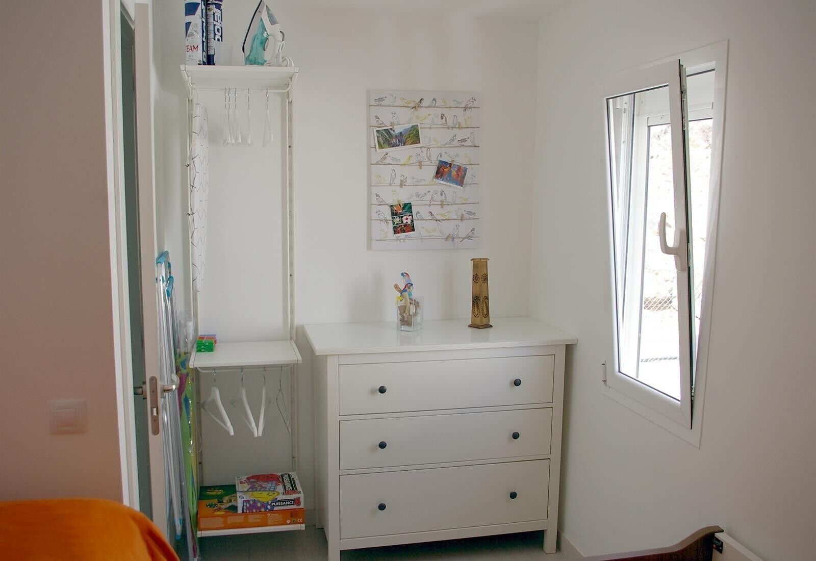 A room with a white dresser, a window with a view, and a door leading to another room.