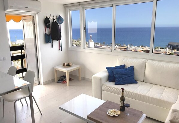 A modern living room with a white sofa, a small table, and a dining area.