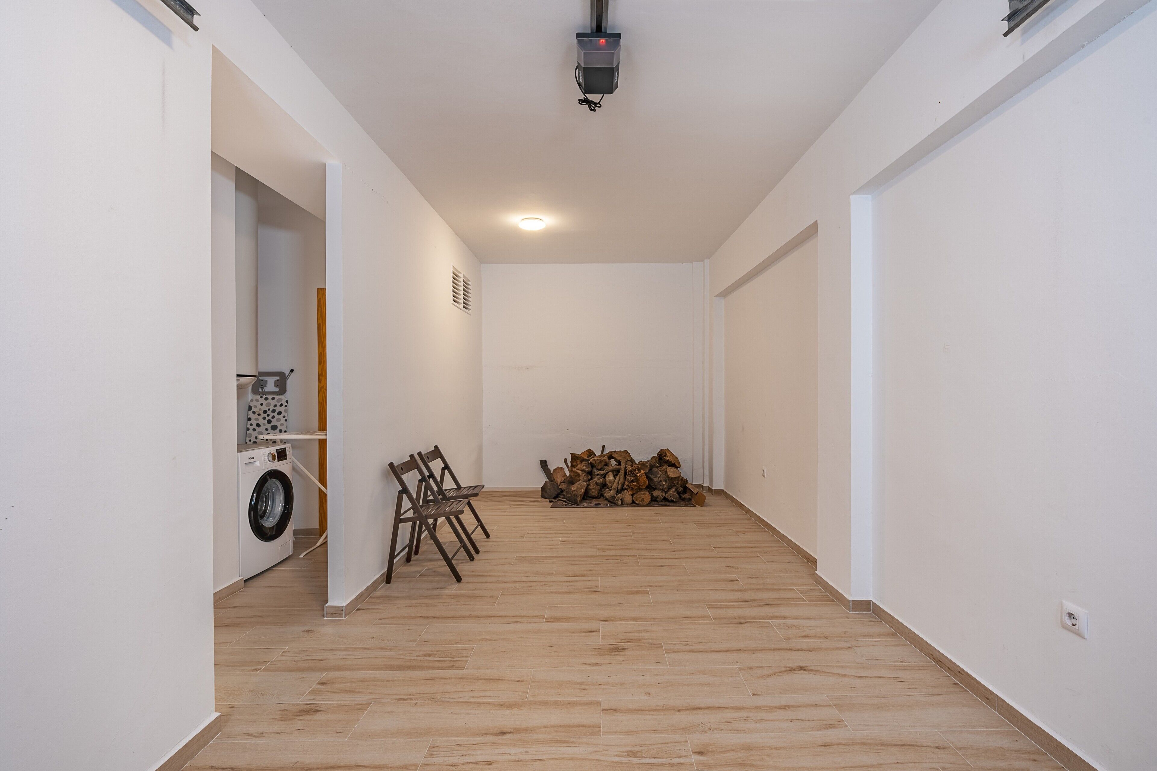 Un couloir où l’on trouve une machine à laver, des chaises et une pile de bois de chauffage.