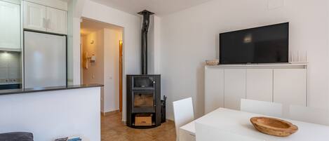 A compact kitchen with white cabinets, a built-in TV, and a wood-burning stove.