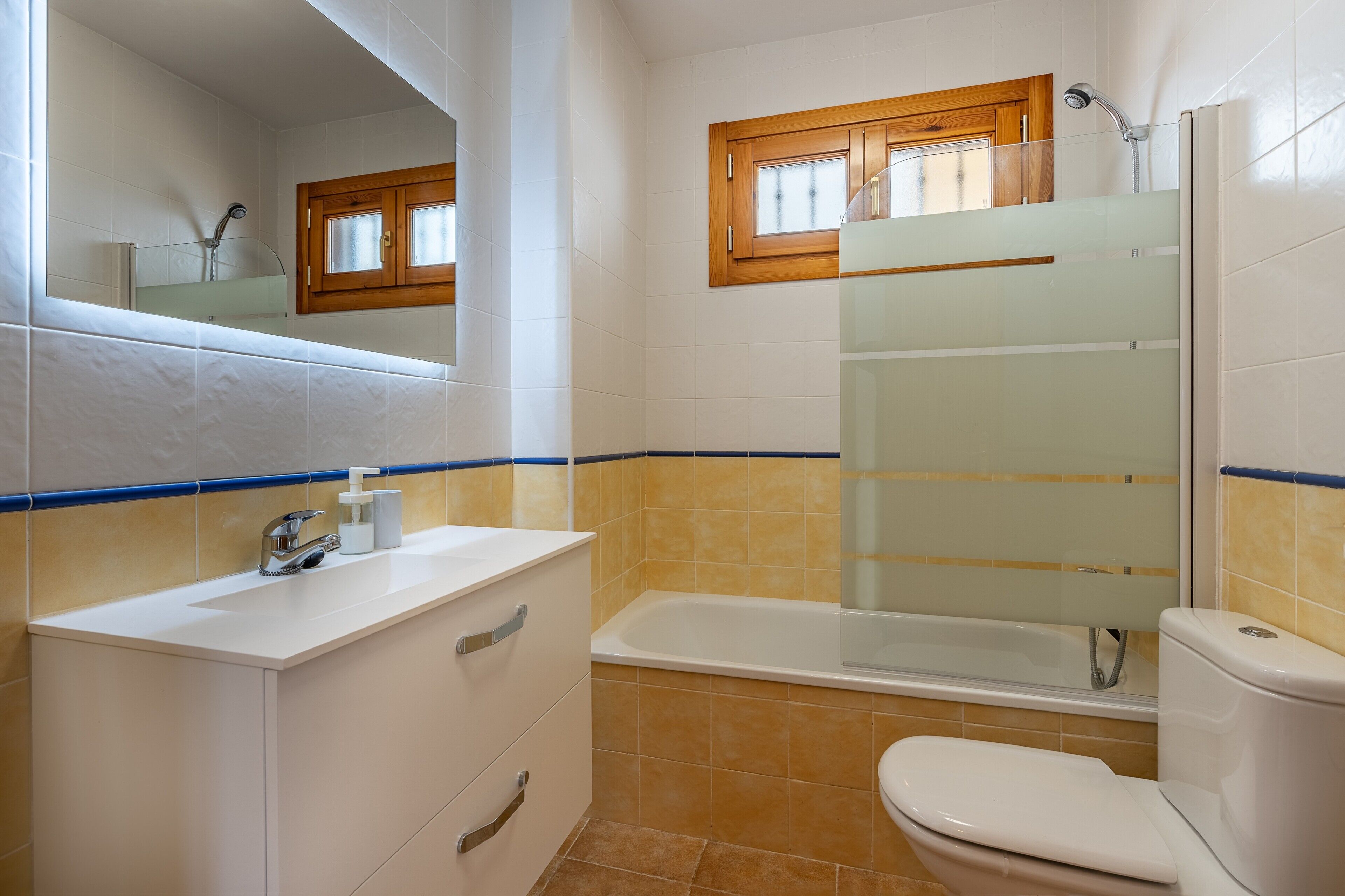 Un baño con bañera, inodoro, lavabo y una ventana sobre la bañera.