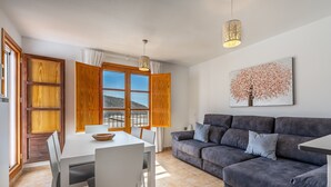 Una sala de estar moderna con un sofá gris, una mesa de comedor con sillas y un gran ventanal con persianas de madera.