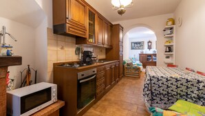 Una cocina compacta con armarios de madera, un microondas, una estufa y un comedor con mantel estampado.