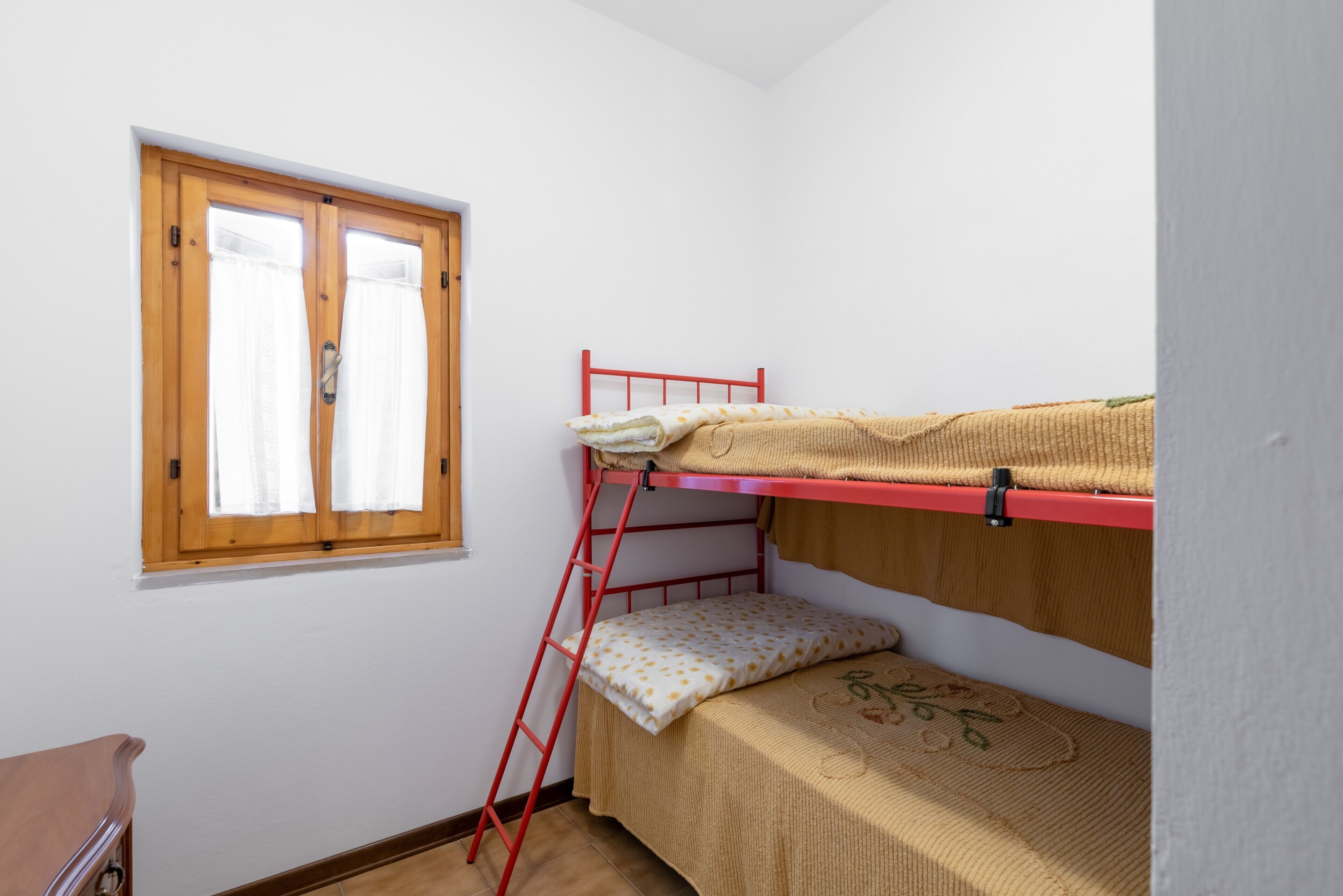Une chambre avec un lit superposé, une échelle en bois, une fenêtre avec des rideaux et une petite table en bois.