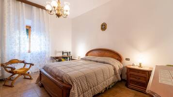 A bedroom with a wooden bed, a nightstand, a chair, a sewing machine, and a chandelier.