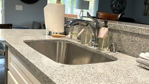 A kitchen with a granite countertop, stainless steel sink, and modern faucet. - Welcome to The 255 — Your Home Away from Home (Parkland)