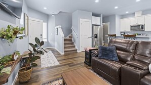 A modern living room with a brown leather sofa, a wooden coffee table, and a staircase leading to the kitchen. - Welcome to The 255 — Your Home Away from Home (Parkland)