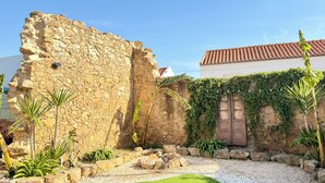 Un mur de pierre, une porte en bois et un bâtiment avec un toit recouvert de tuiles rouges.
