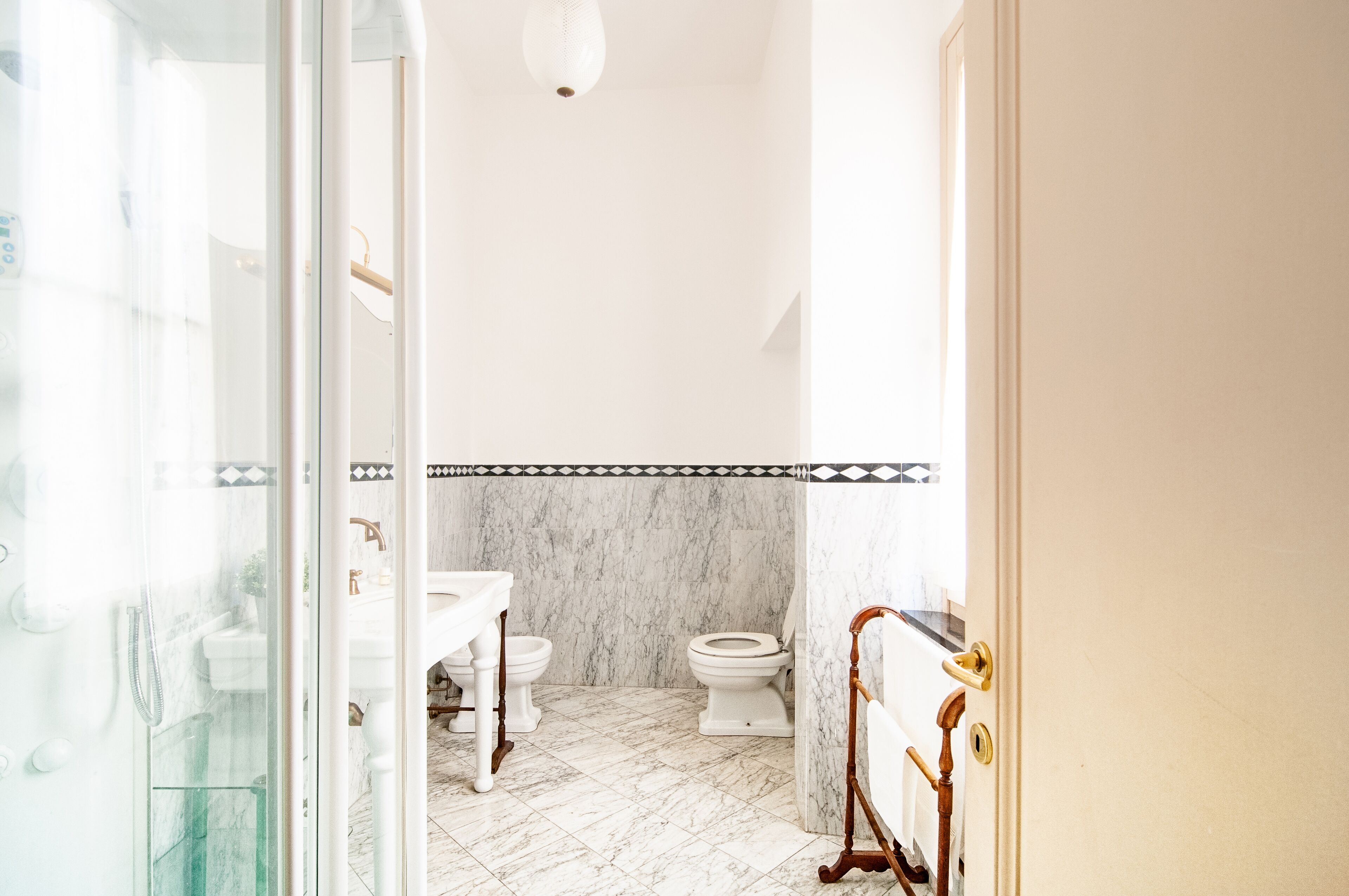 A bathroom with a white sink, two toilets, a shower area, and a marble-tiled floor.