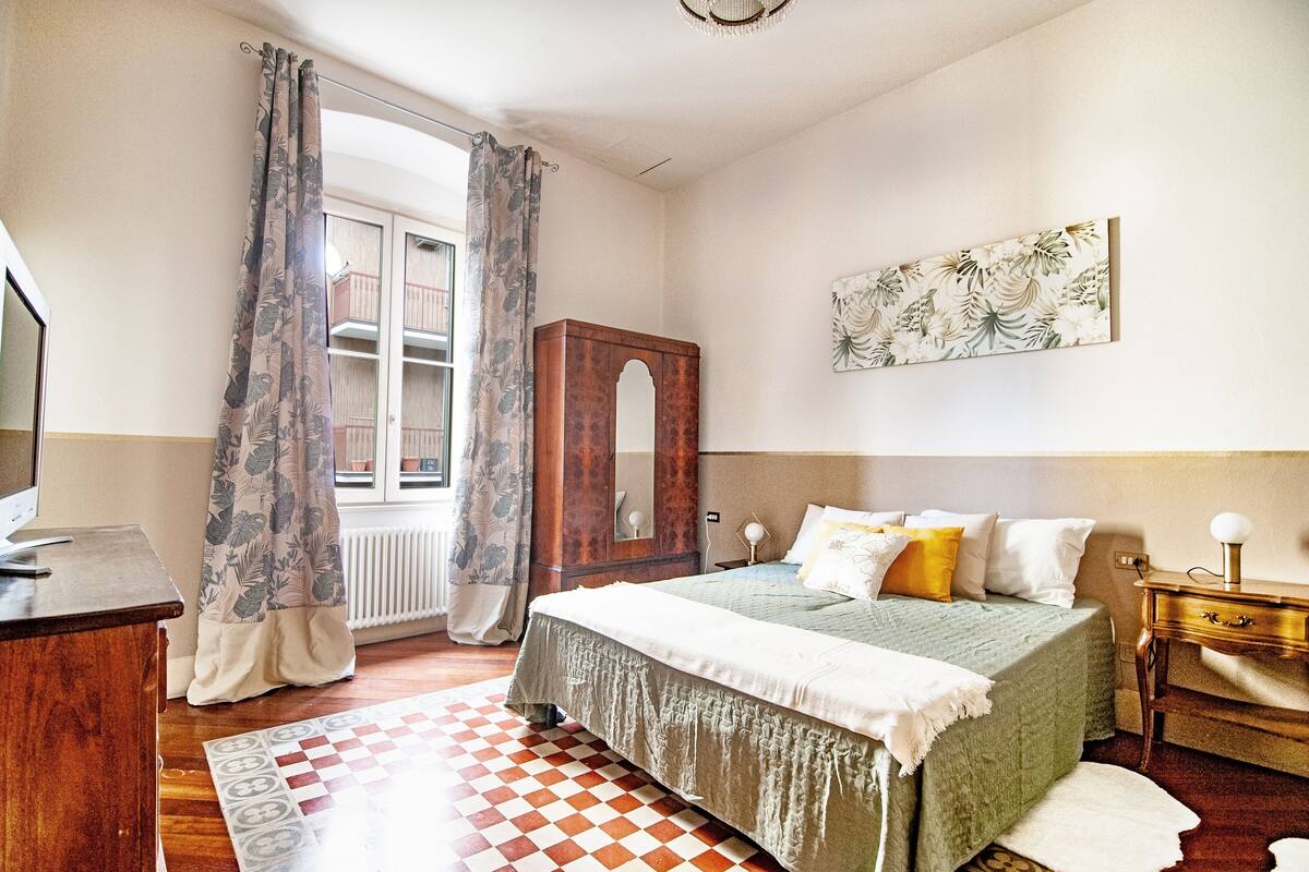 A bedroom with a bed, a wooden wardrobe, a desk, and a radiator.