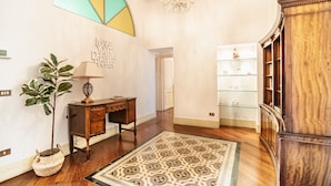 Un couloir avec un bureau en bois, une plante en pot, un lustre et un tapis à motifs.
