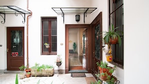 Une entrée soignée, avec une porte en bois, des plantes en pot et un sol carrelé.