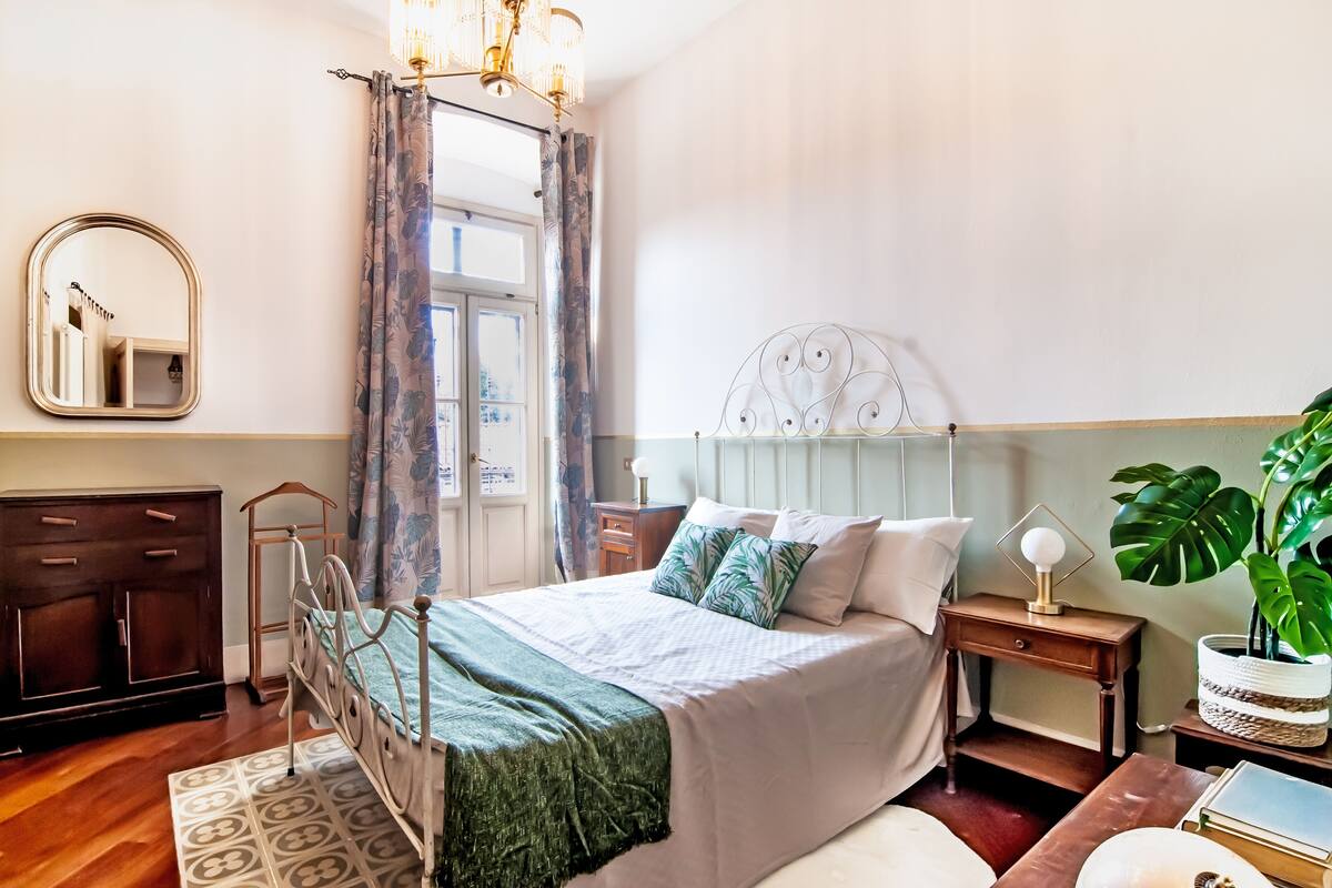 A bedroom with a bed, a nightstand, a mirror, a wardrobe, and a potted plant.
