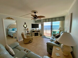 A spacious living room with a large sofa, a recliner, a television, and a ceiling fan. There is a balcony with a view of the ocean. - Gorgeous and Gulf Front! Pool! (Gulf Shores)