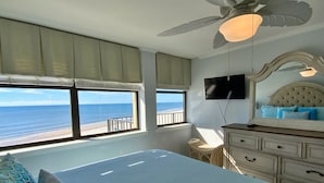 Une chambre avec un lit, une télévision, un ventilateur de plafond et une vue sur la plage.