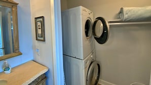 Un espace buanderie équipé d’un lave-linge et d’un sèche-linge à chargement frontal, d’un porte-serviettes, d’un miroir et d’un tableau encadré accroché au mur.