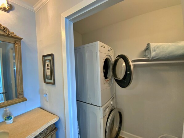 A laundry area with a front-loading washer and dryer, a towel rack, a mirror, and a framed picture on the wall.